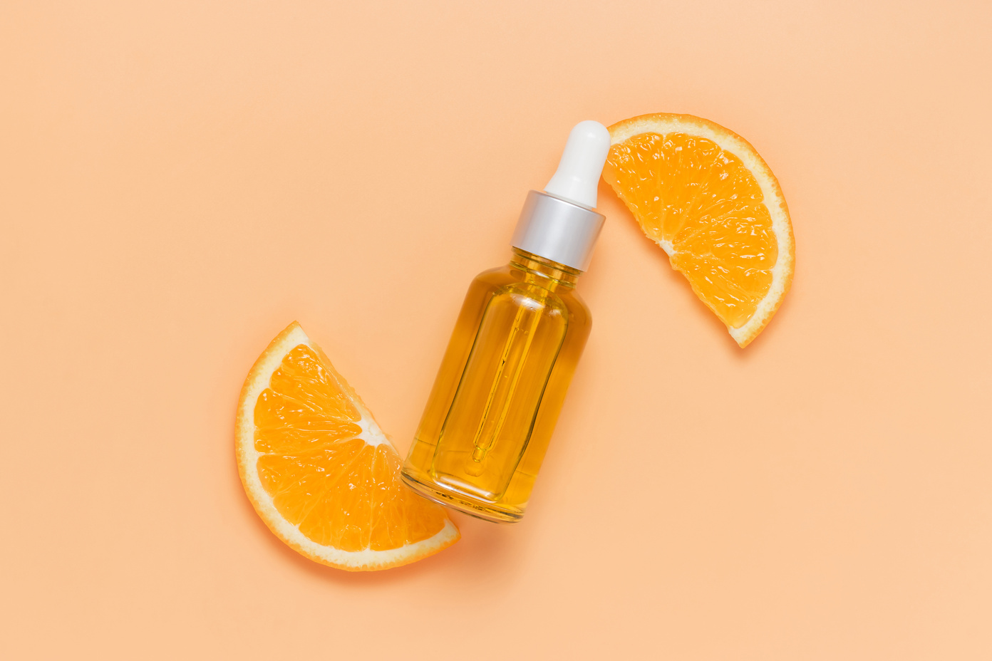 Facial oil bottle with vitamin C on sliced orange top view
